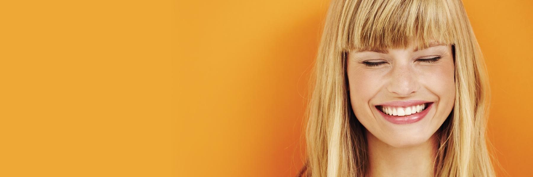 Blonde woman smiling against a solid orange background